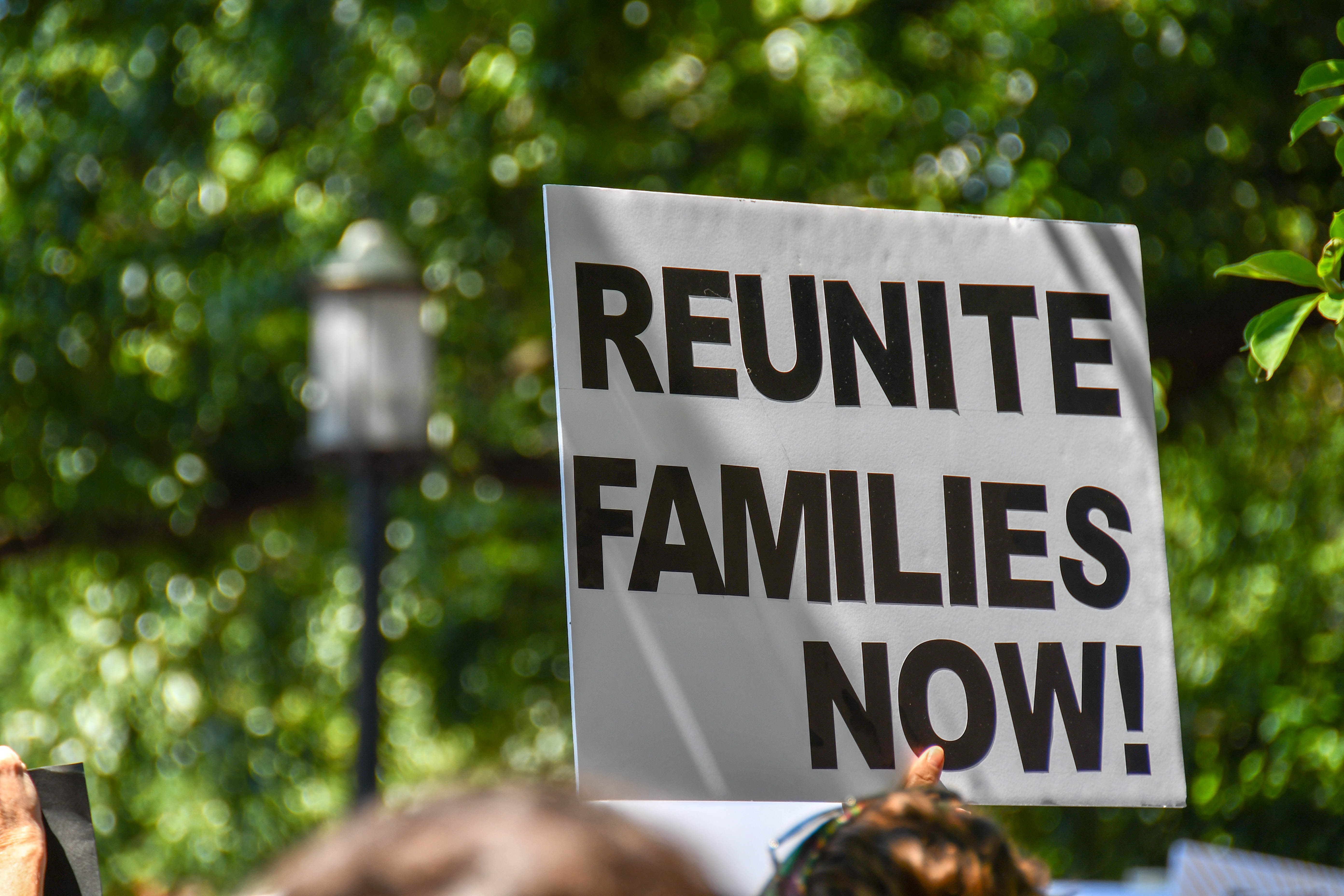 White sign with black text that reads: Reunite Families Now!