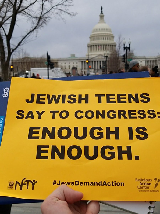 Hand holding sign in front of Capitol building that says Jewish Teens Say to Congress: Enough is Enough